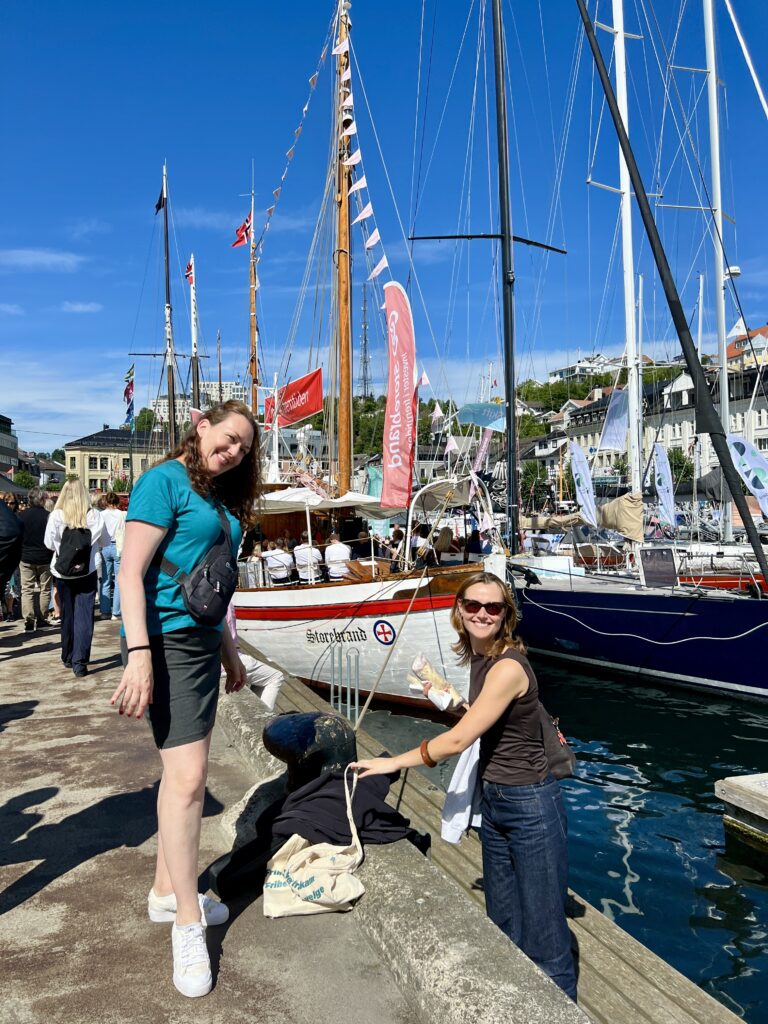 Fotografi av to kvinner ved en brygge. I bakgrunnen ser du to seilbåter.
